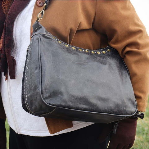 close up of a woman carrying a  gray concealed carry HOBO purse in soft vintage leather with dark chrome rivets, RFID protection, dual zip compartments, CCW access for Glock 26 or Sig P320, slash-proof shoulder strap, and left/right hand draw compatibility.