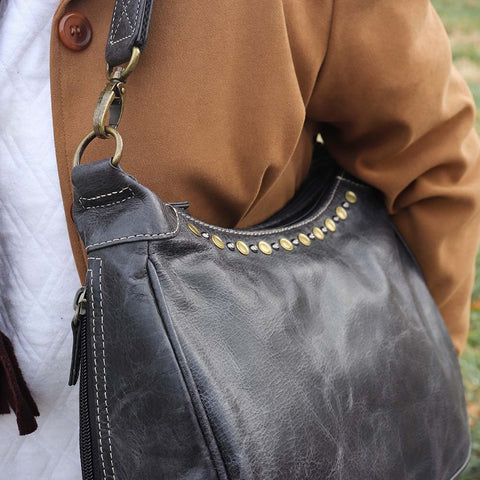 woman from the side with a gray concealed carry HOBO purse in soft vintage leather with dark chrome rivets, RFID protection, dual zip compartments, CCW access for Glock 26 or Sig P320, slash-proof shoulder strap, and left/right hand draw compatibility.